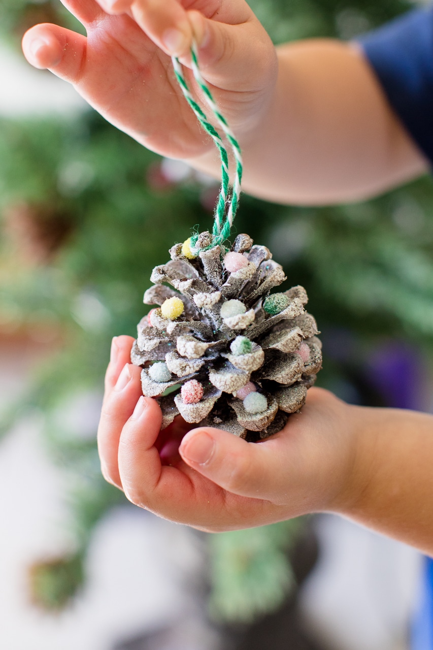 snowy pinecone ornament in childs hand