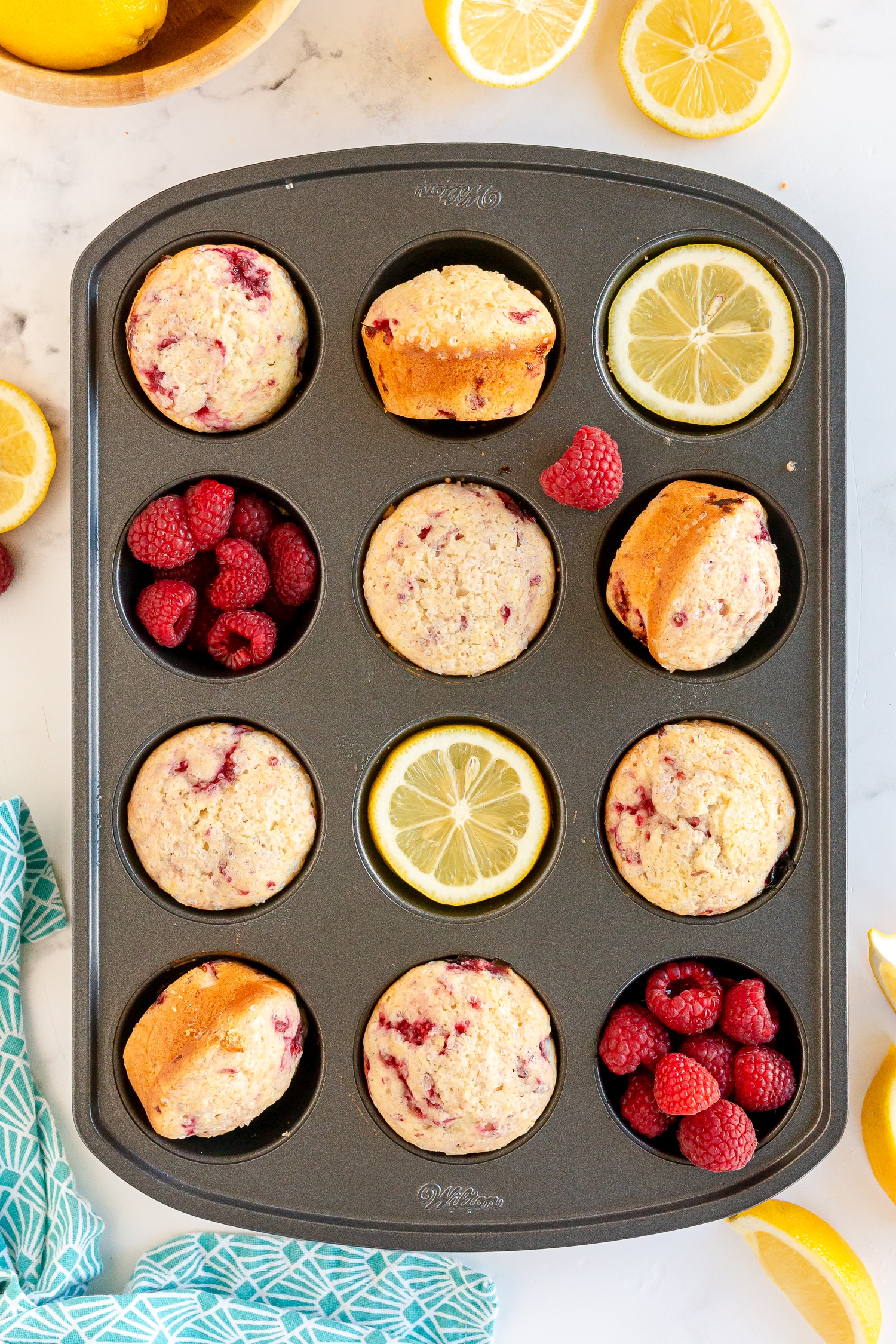 lemon raspberry muffins in muffin tin with raspberries and lemon garnishes