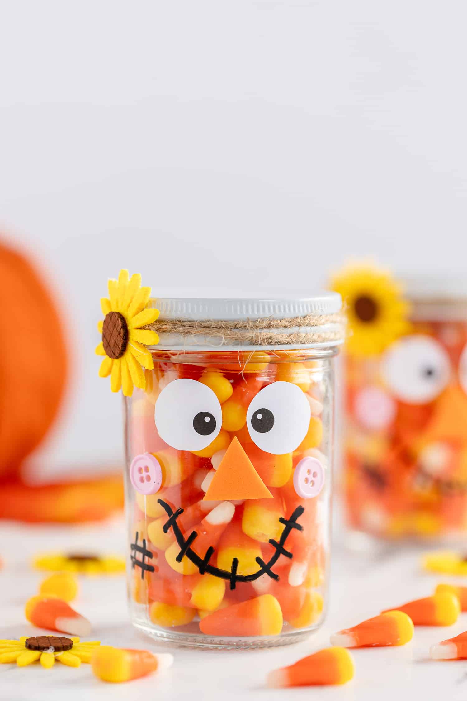 Mason Jar Scarecrow with pumpkin in the background on craft table