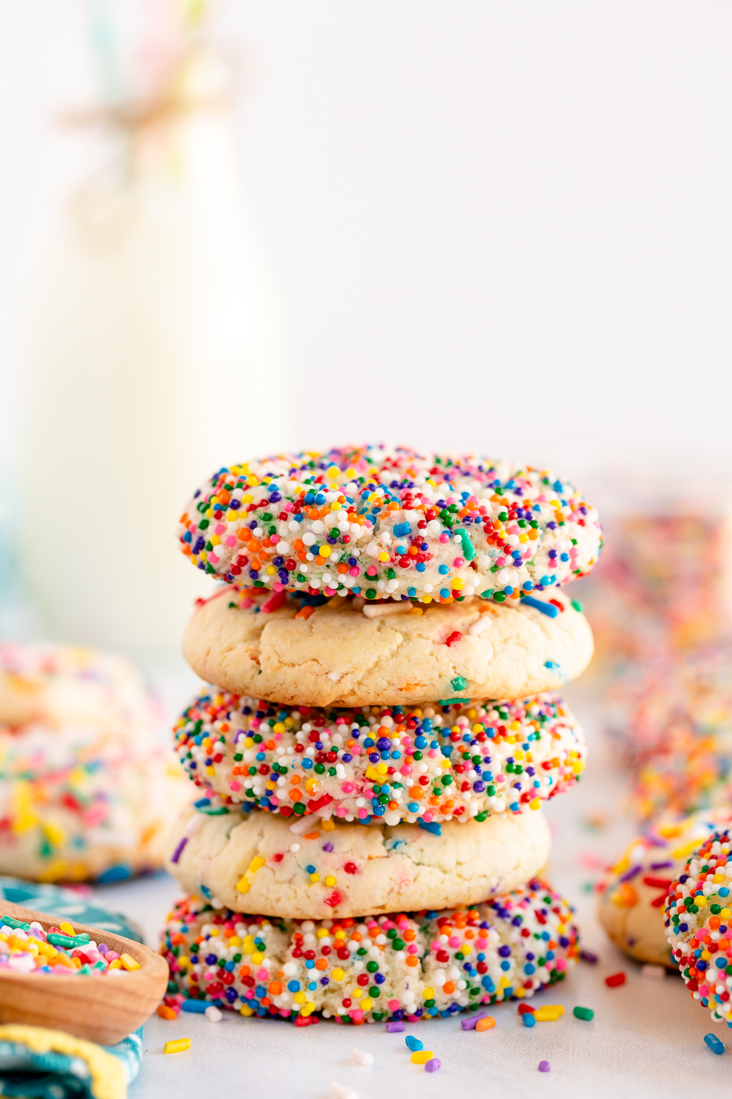 sprinkle covered cookies stacked on counter with milk