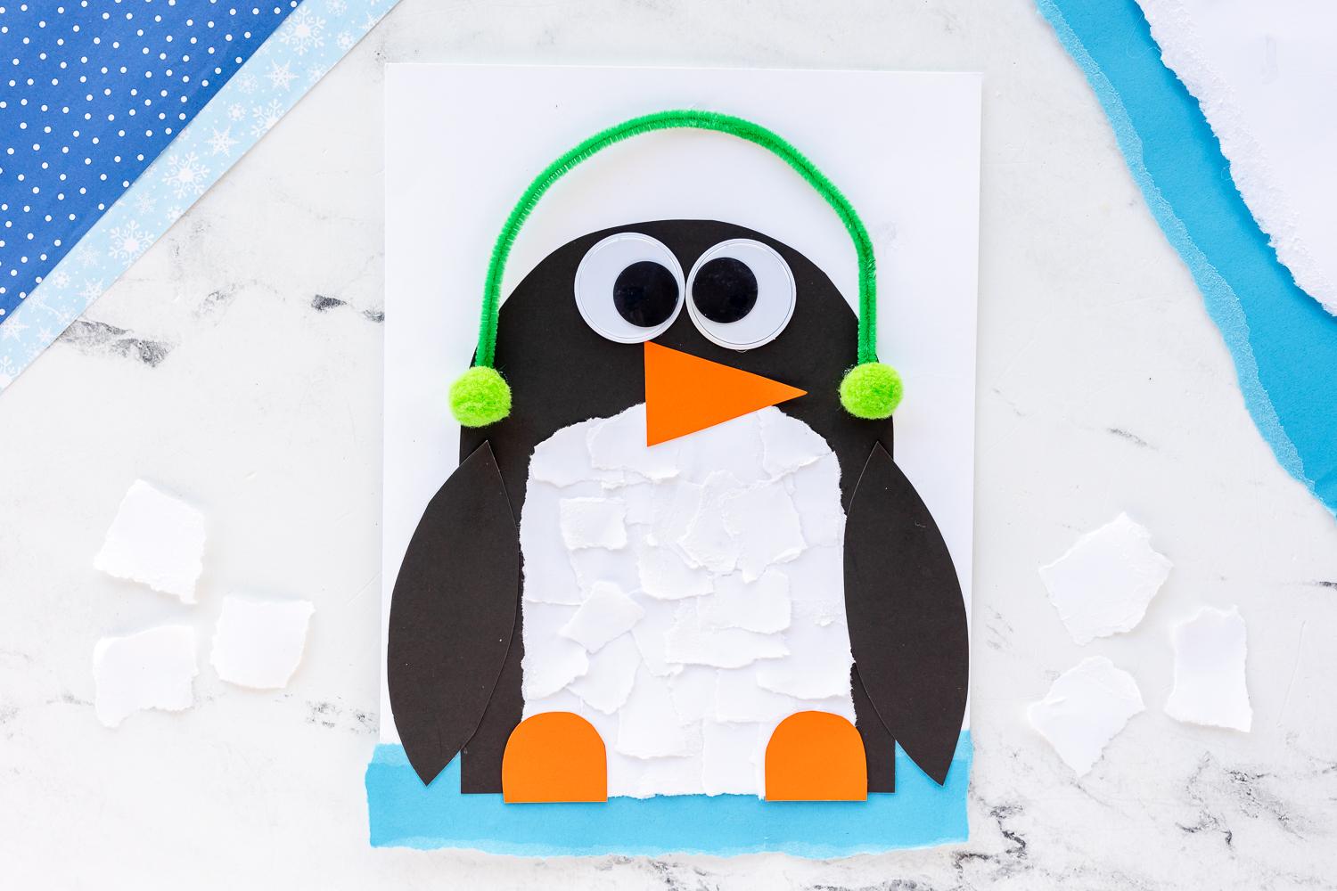 torn paper penguin craft on counter with ripped white paper next to it