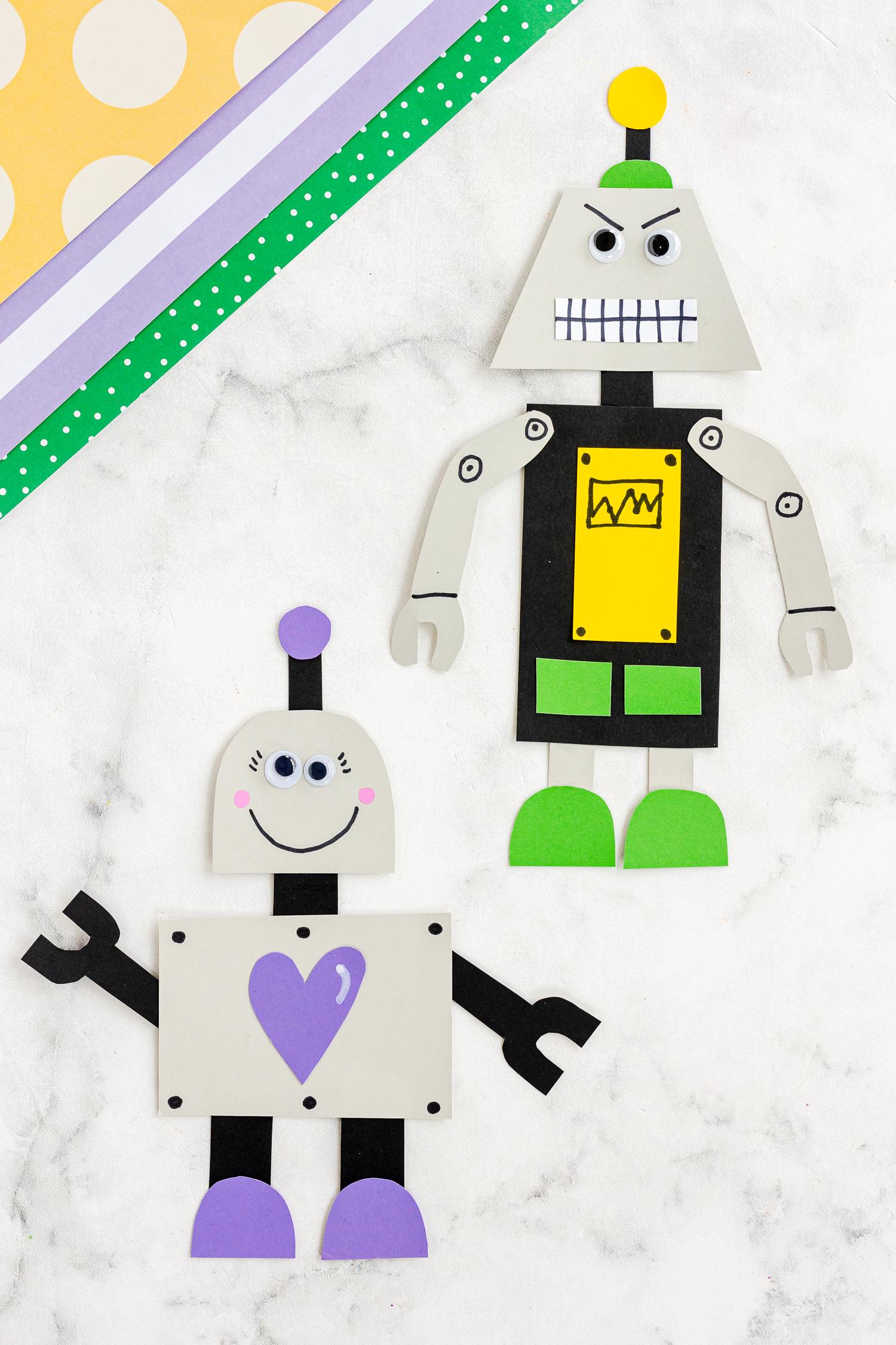 two paper robots on craft counter with colored cardstock in corner