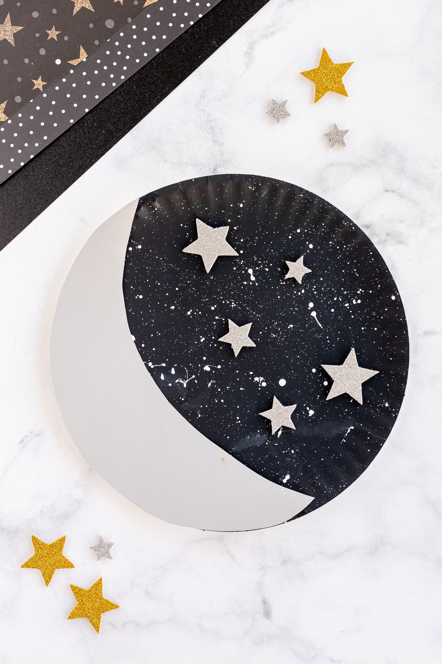 paper plate moon with stars nearby on craft counter