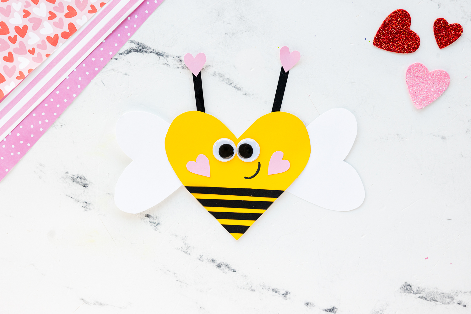 heart shaped bee craft on counter with glitter hearts