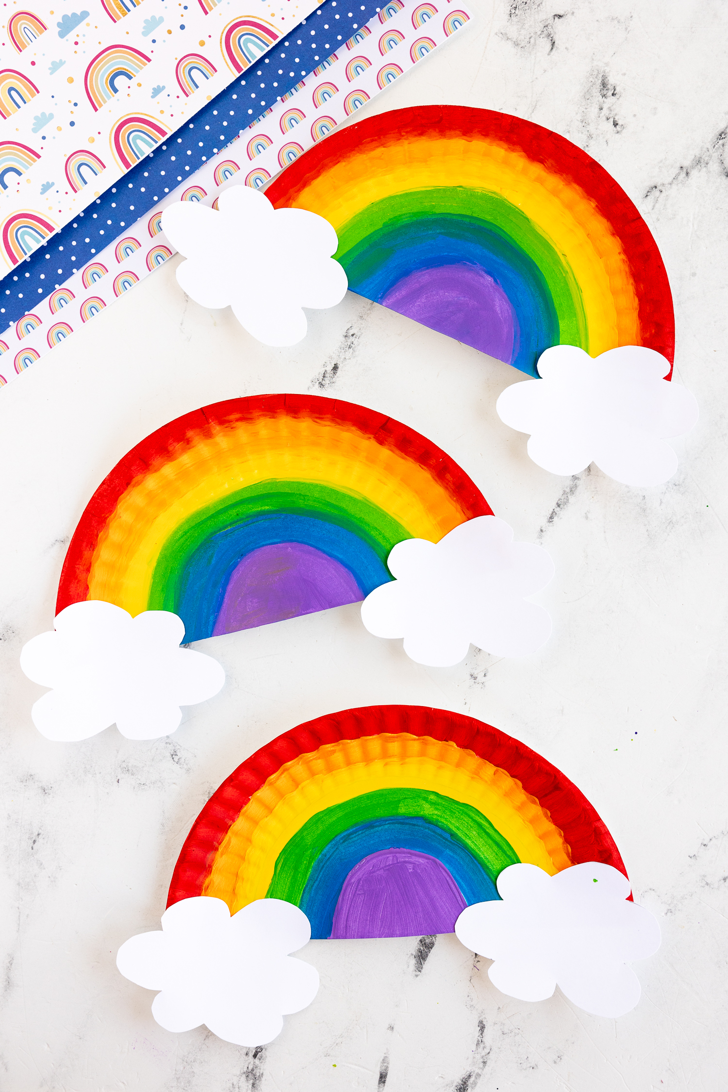 three painted paper plates in rainbow colors with paper clouds attached