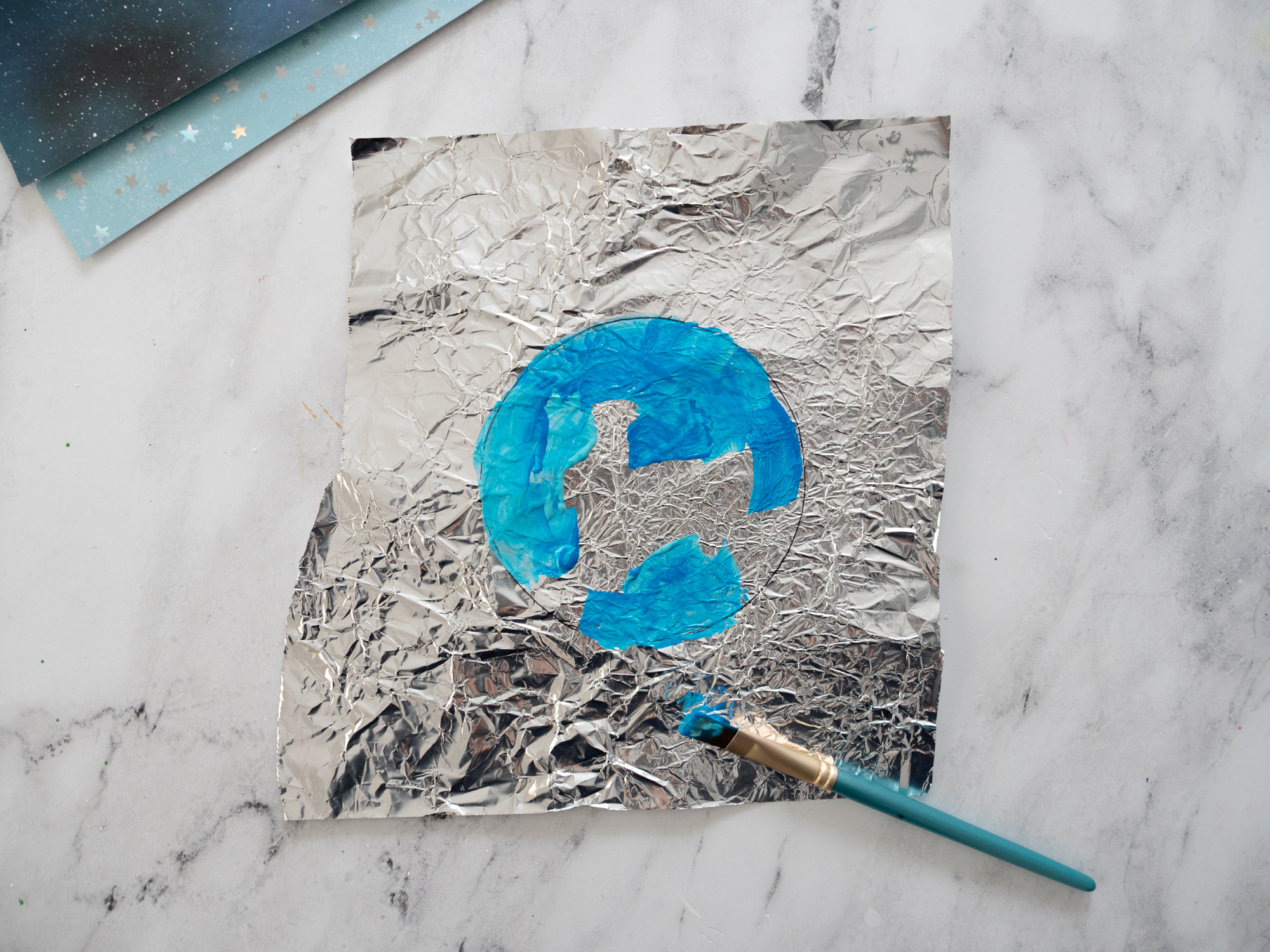 painting blue and green paint onto foil for Earth Day craft