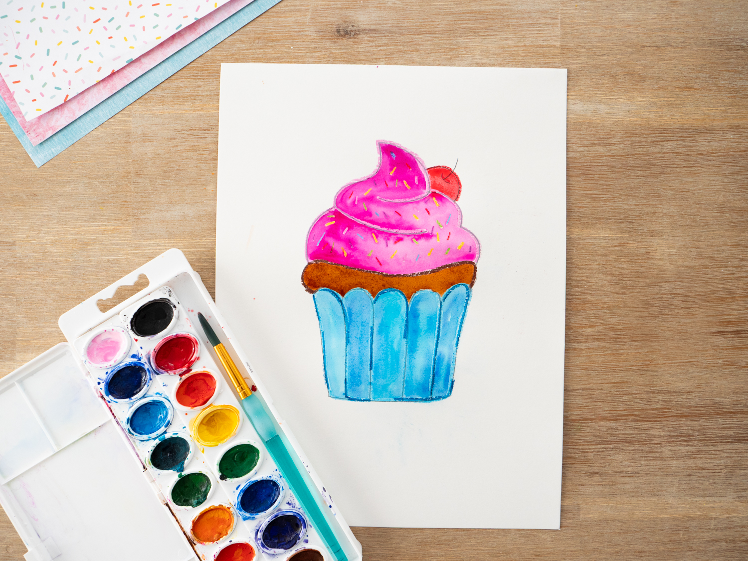 Kids painting watercolor over oil pastel cupcake drawing to create resist effect.