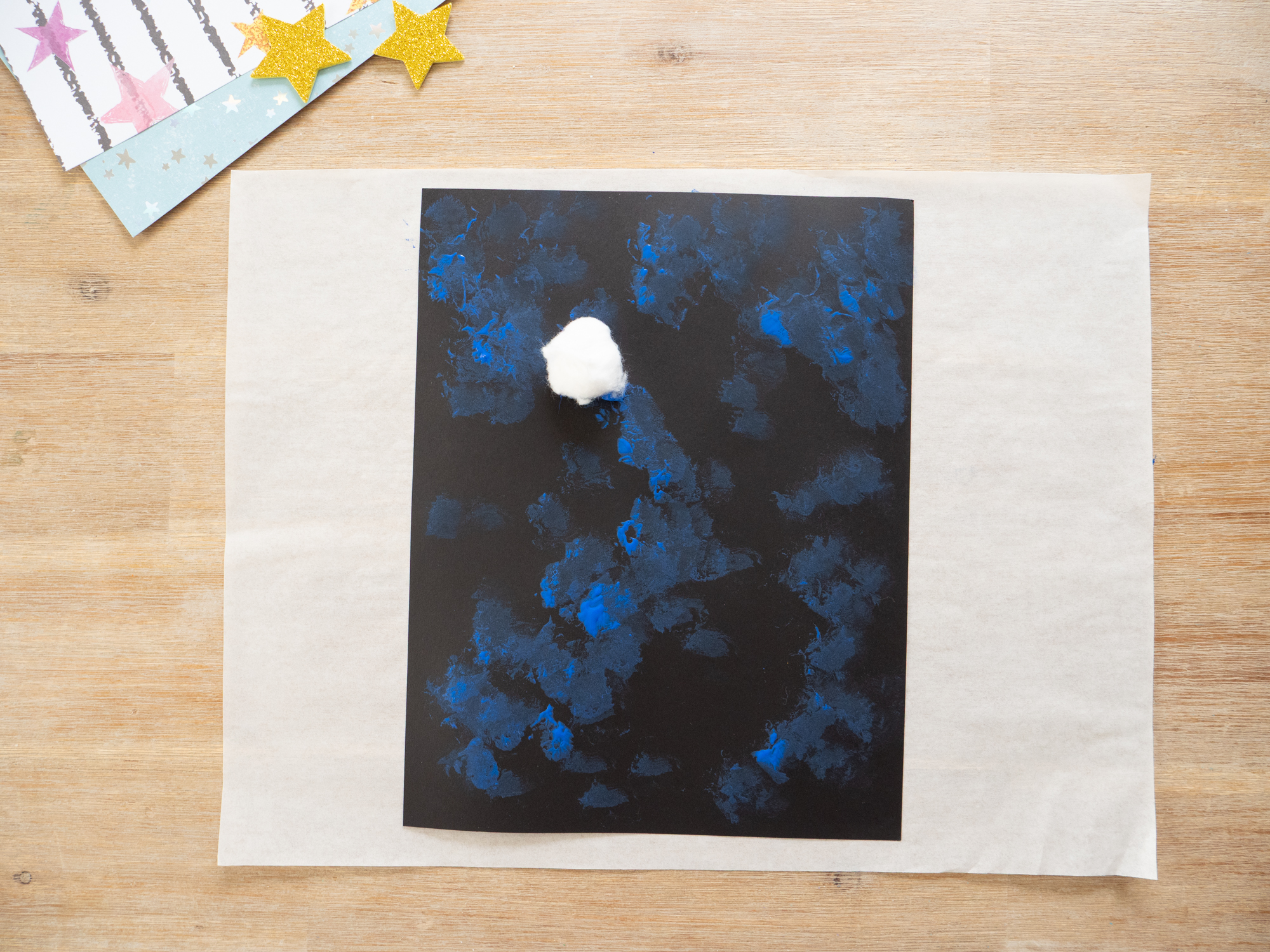 kids dabbing paint with cotton balls to make galaxy background