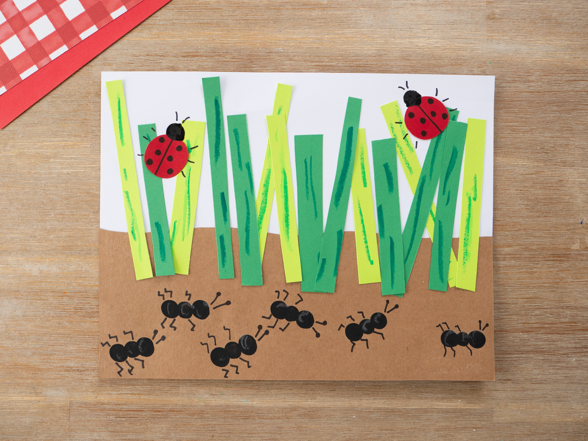 Finished fingerprint ant craft with paper grass, ladybugs, and marching ants