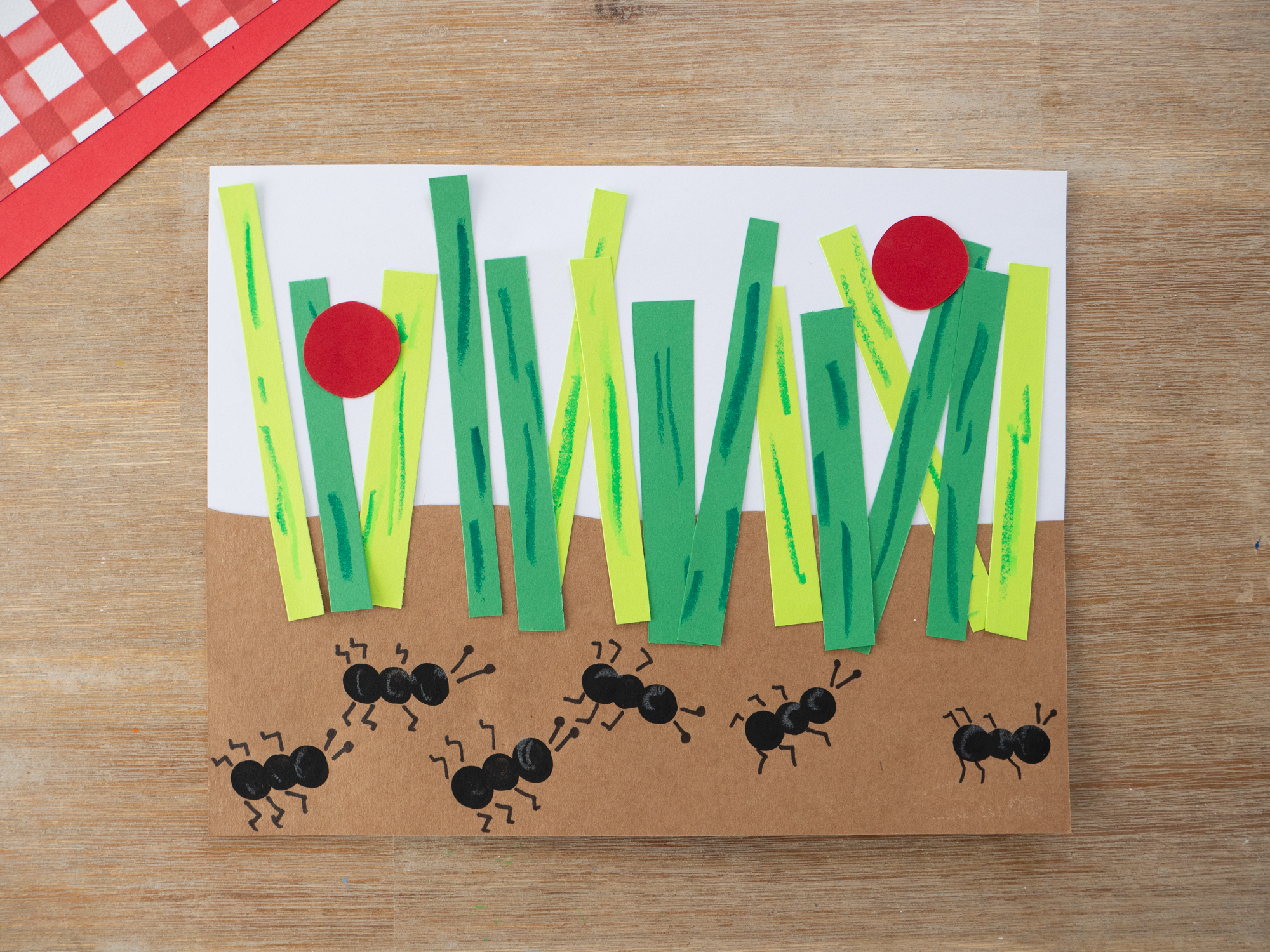 Red paper ladybugs added to the grass on a fingerprint ant craft for kids