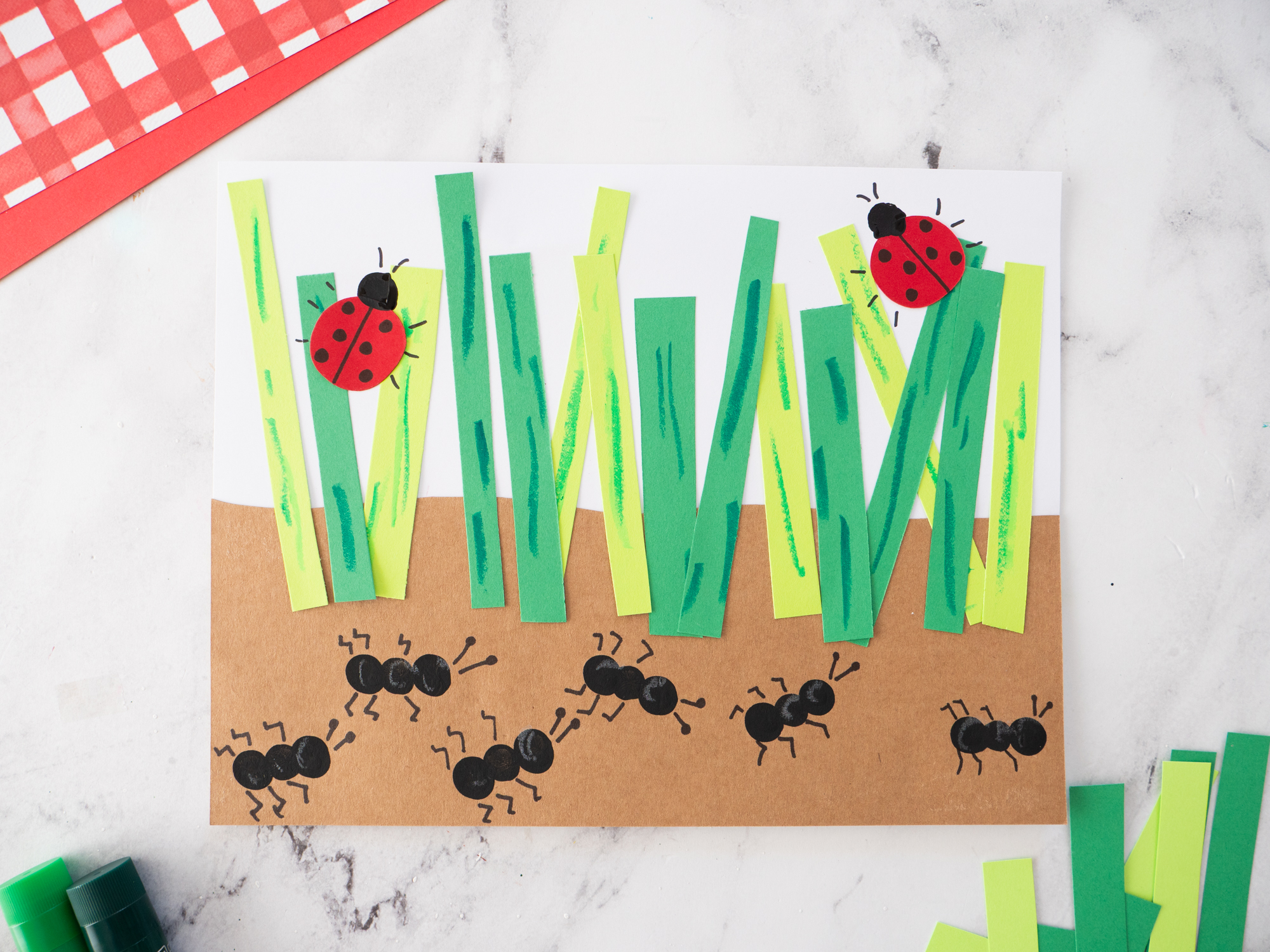 Fingerprint ant craft for kids with paper grass and ladybugs on a garden scene